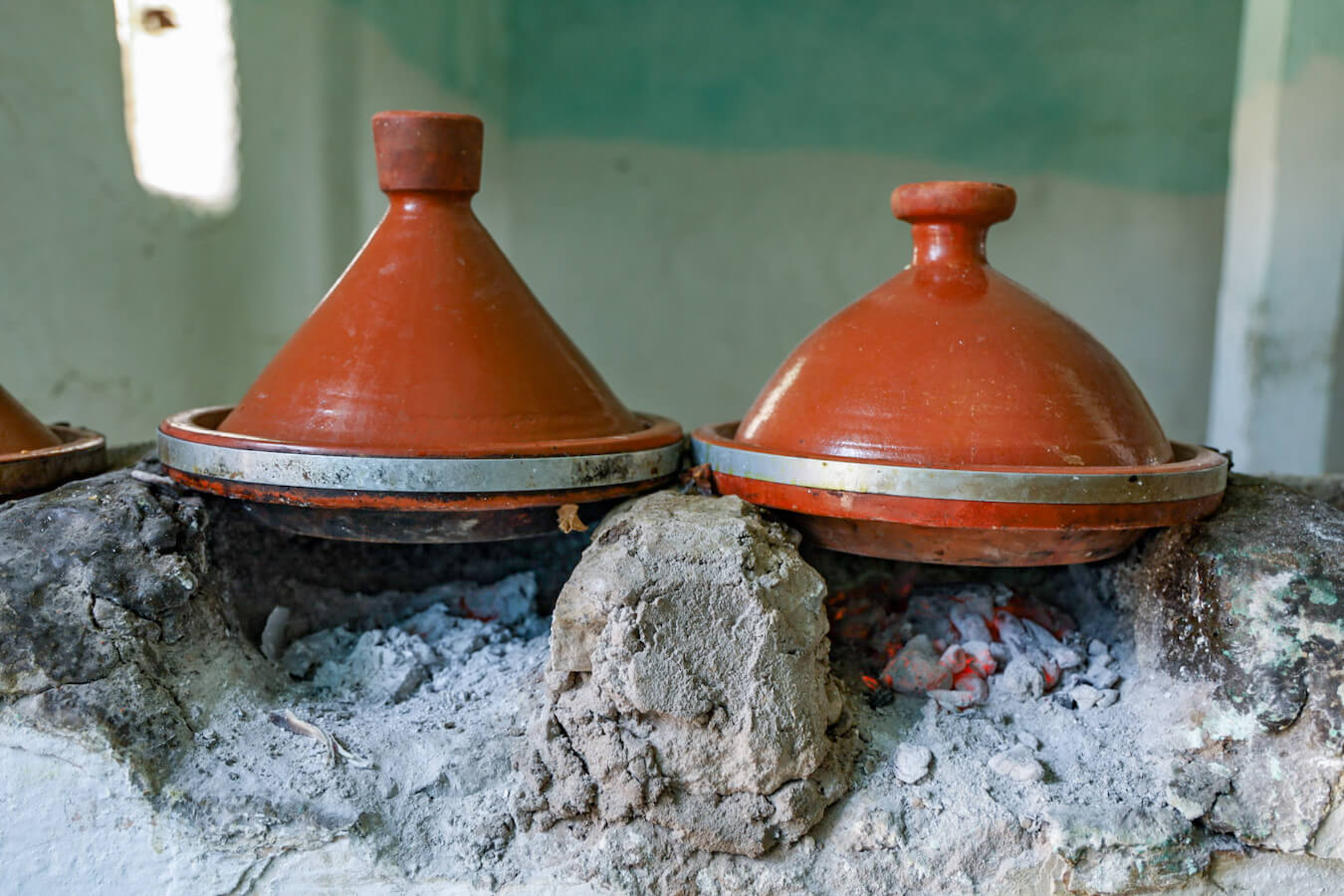 Two clay tagines cook over coals in Morocco - an example of an economical and budget way to eat while travelling on a Morocco road trip.
