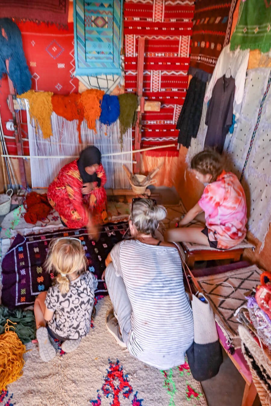 A family watch a Moroccan woman make a carpet in her shop in Ait Ben Haddou, Morocco.