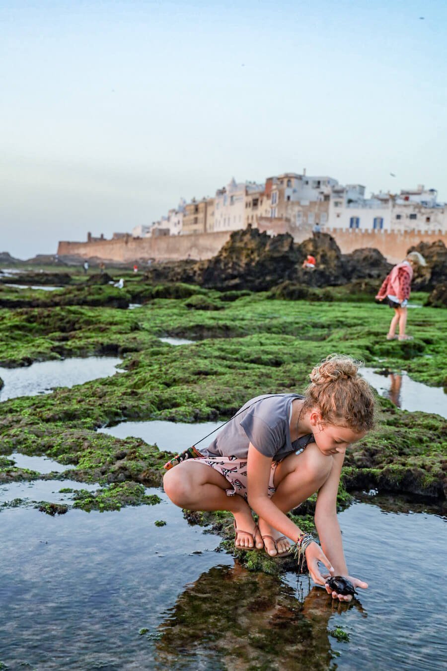 Children look through rock pools in Essaouira, beyond the rampart walls on an itinerary for 14 days in Morocco