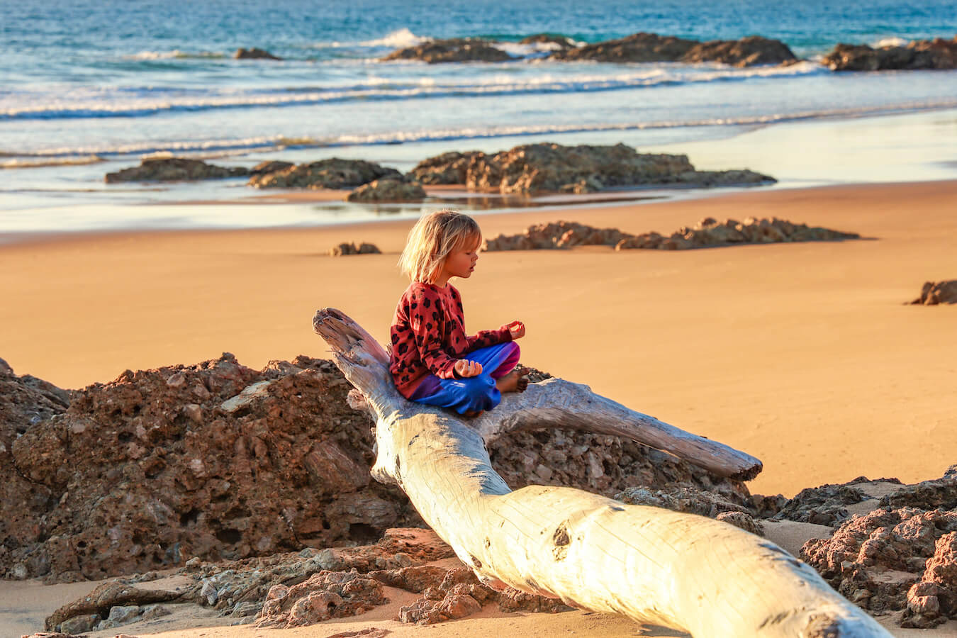 A child sits on a log on the beach meditating in Agnes Water and 1770