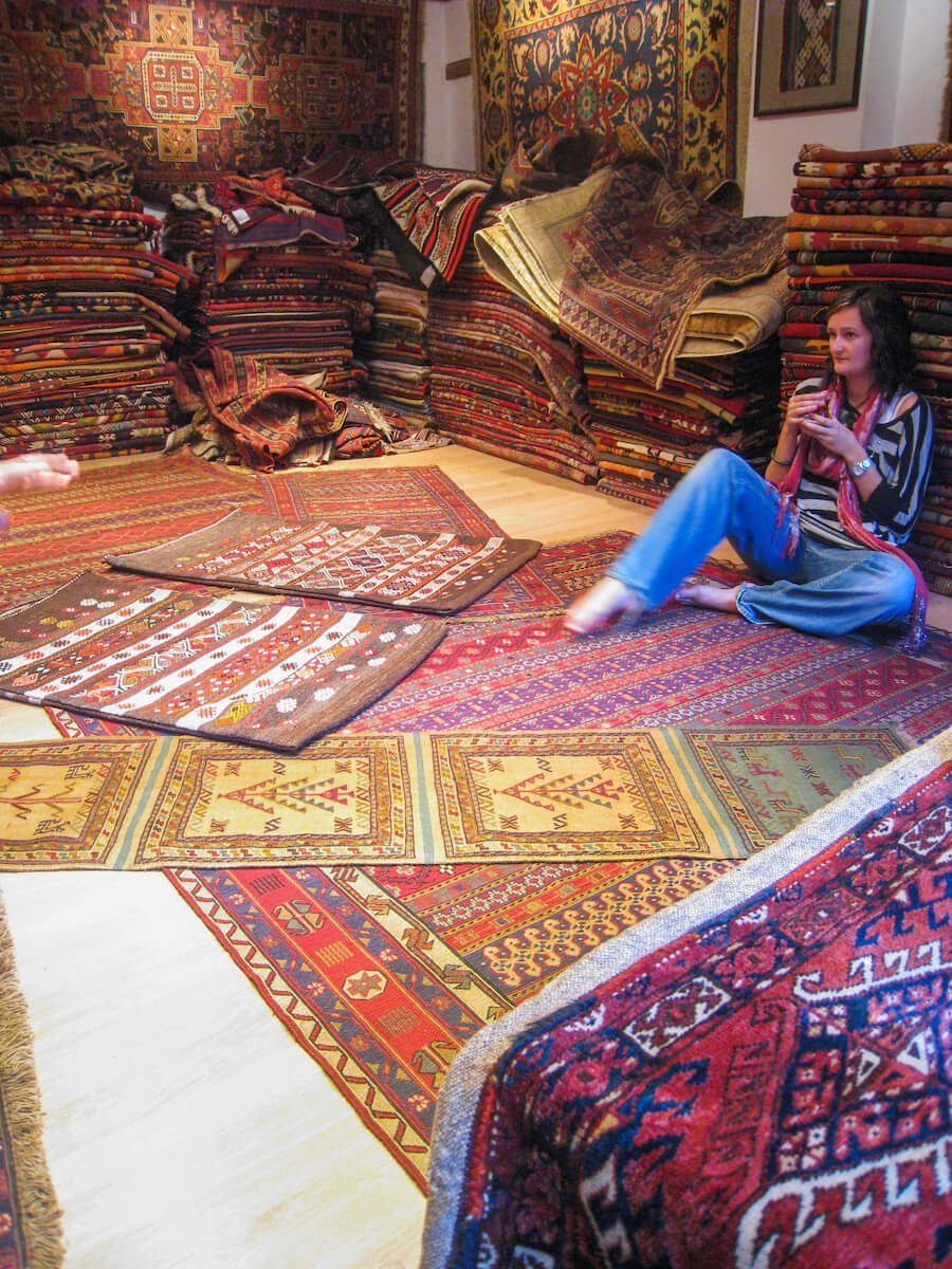 Lady shops for carpets in Istanbul Turkey with a cup of Turkish tea.