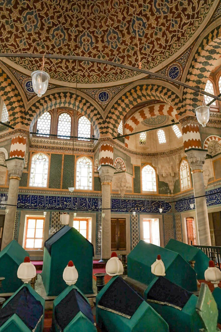 The tombs inside the Sultan's Tombs are lined in a row below an ornately decorated room.