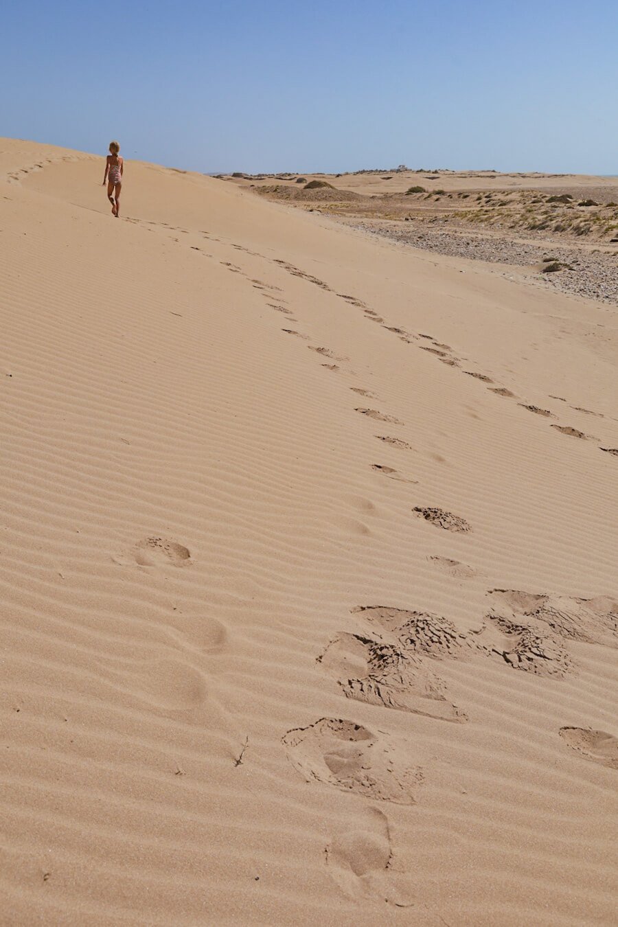A child walks along the beach the long white sand dunes in Essaouira on a beach and surf vacation.
