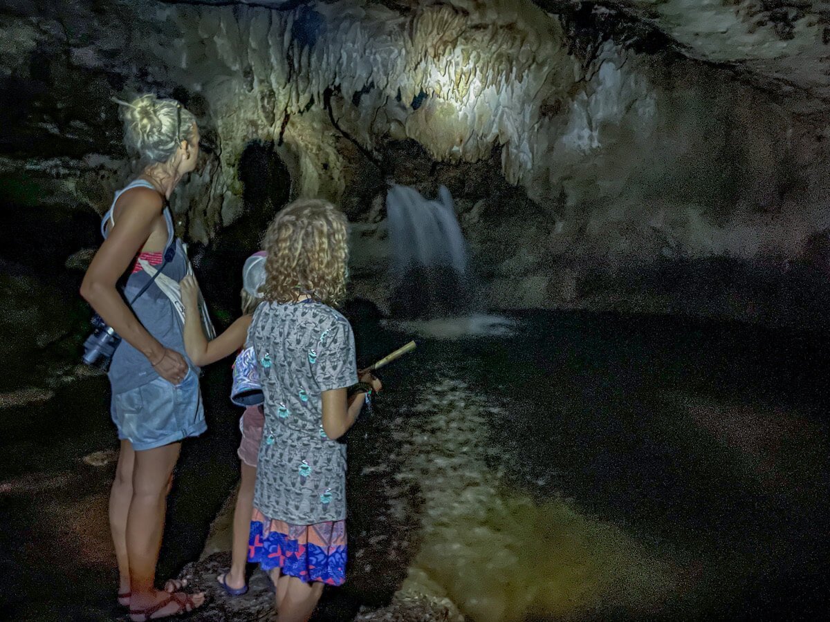A mother and her two daughters, standing beside the small pool in a cave / grotto. 