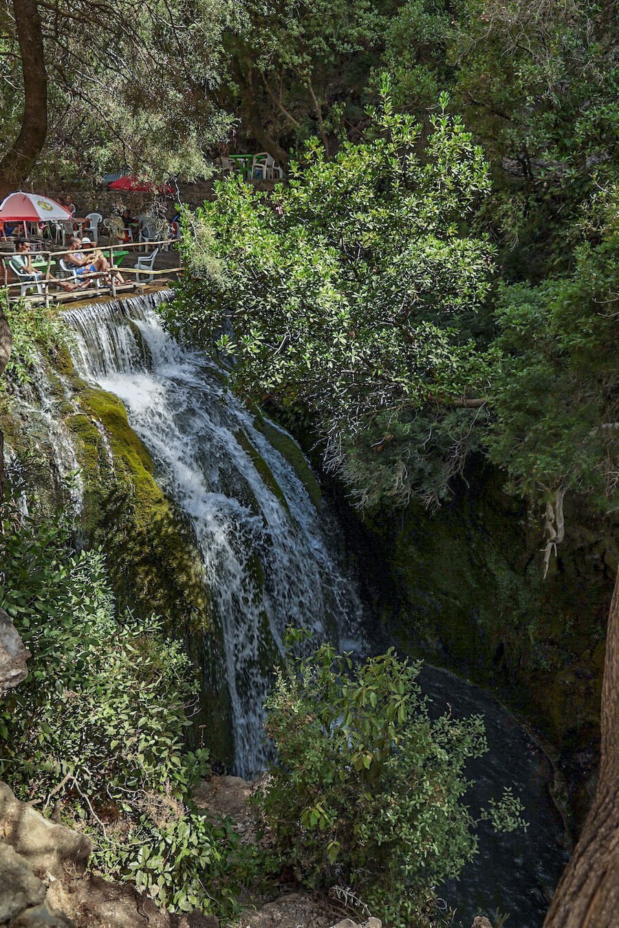 Holiday makers sit at the top of the petit or small waterfalls of Akchour on a God's Bridge day trip from Chefchaouen.