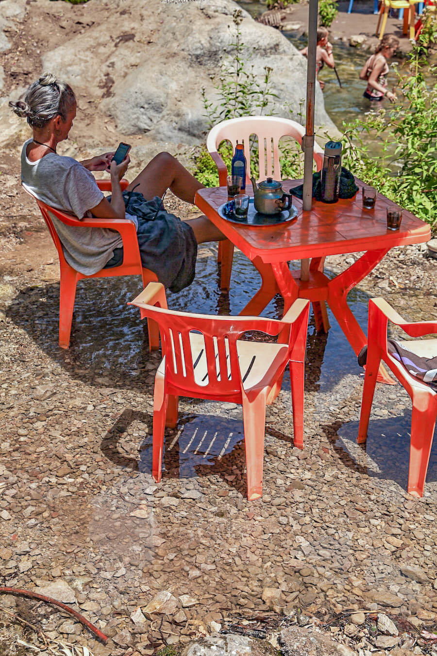 Woman sits at a restaurant table in a river in Morocco - Cuisine Berber in the Akchour valley on the way to God's Bridge