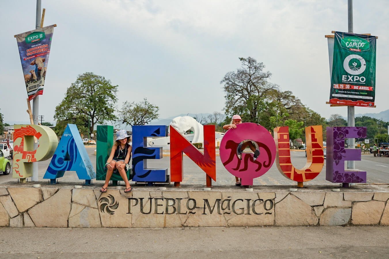 Two young girls stand amounts the letters of the Palenque Pueblo Magico sign.