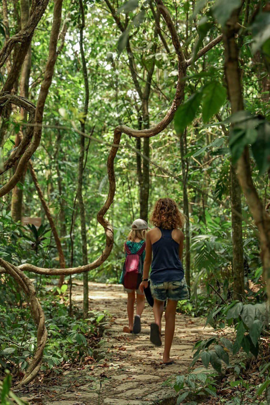 Two young girls, walk along cobbled path, surrounded by thick rain forest in Aluxes Ecopark, Palenque.