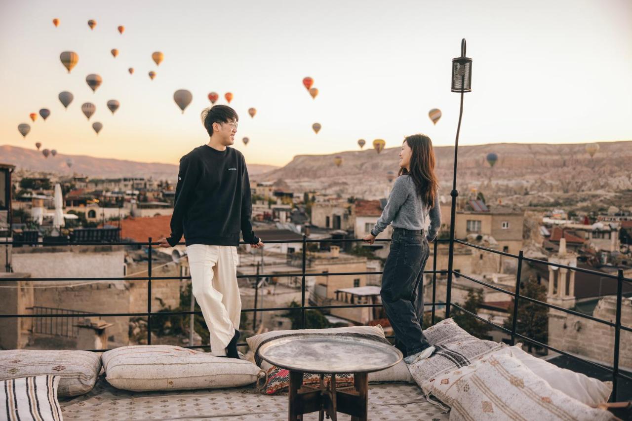 A couple stand on the rooftop terrace of their hotel, admiring the view of hot air balloons flying in the distance in Cappadocia