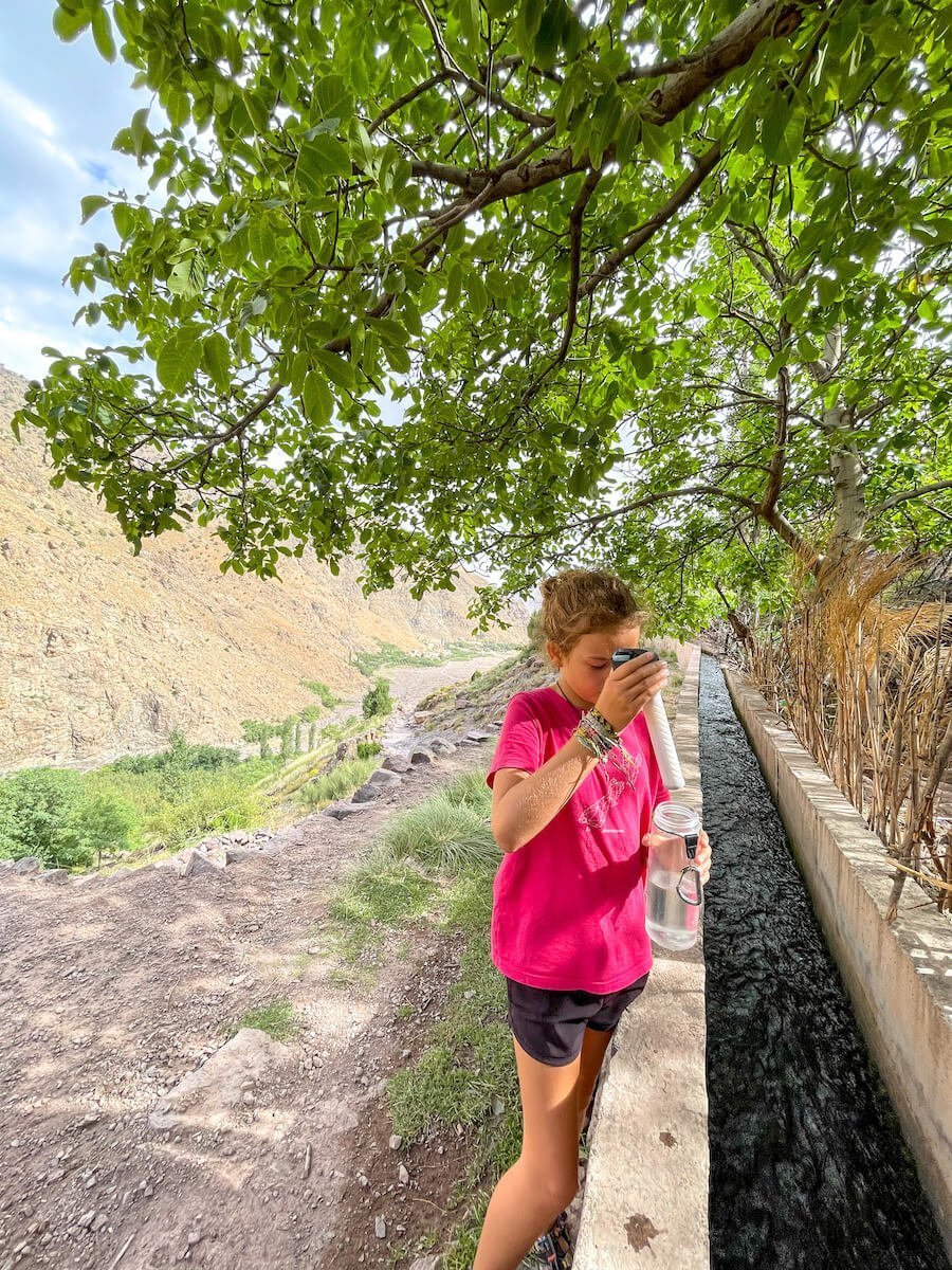 A child fills a lifestraw bottle from a water source in the Atlas Mountains in Morocco