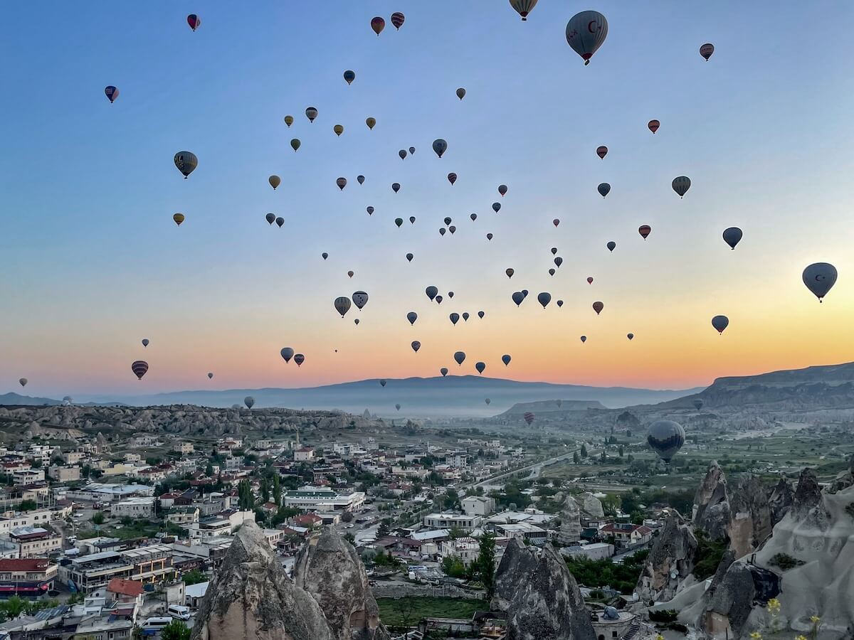 Views over Göreme as many hot air balloons fly over the town and cave hotels below.