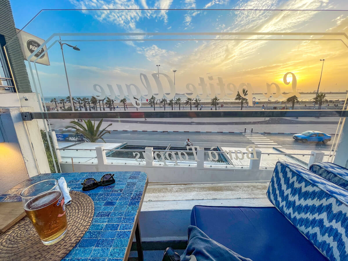 The sunsets over the beautiful beach of Essaouira, a beer sits on a rooftop bar table - The Roof Top Bar Morocco