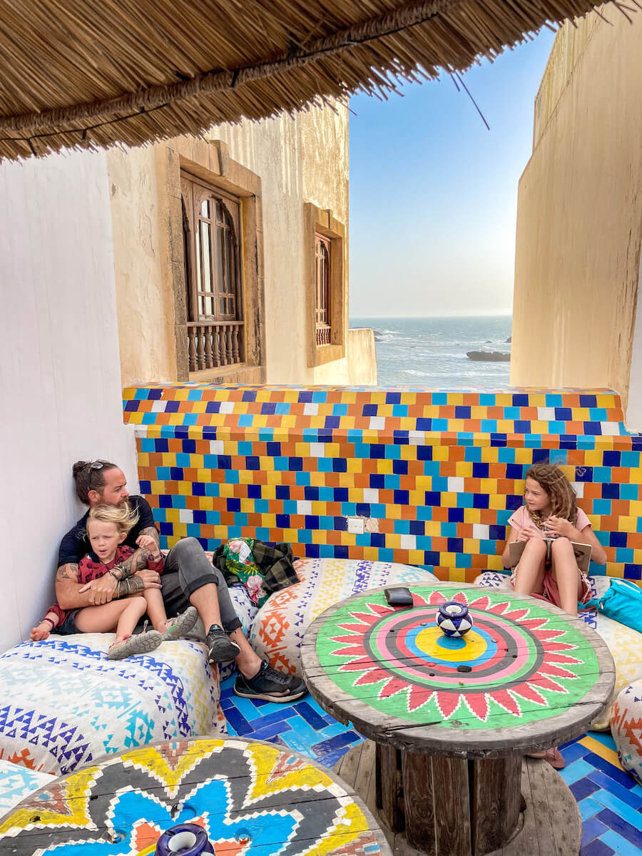 A family sit on rooftop cushions at the bar in Salut Maroc watching the sunset over Essaouira