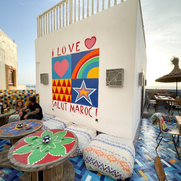 Family sit on cushions on one of the best rooftop bars that serve alcohol in Essaouira, Morocco