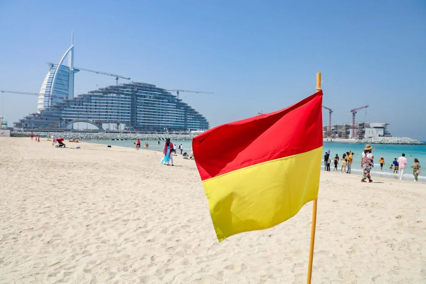 Lifeguard flag flies on free beach in Dubai with Burj al Arab and Marsa Al Arab Hotel under construction in the distance