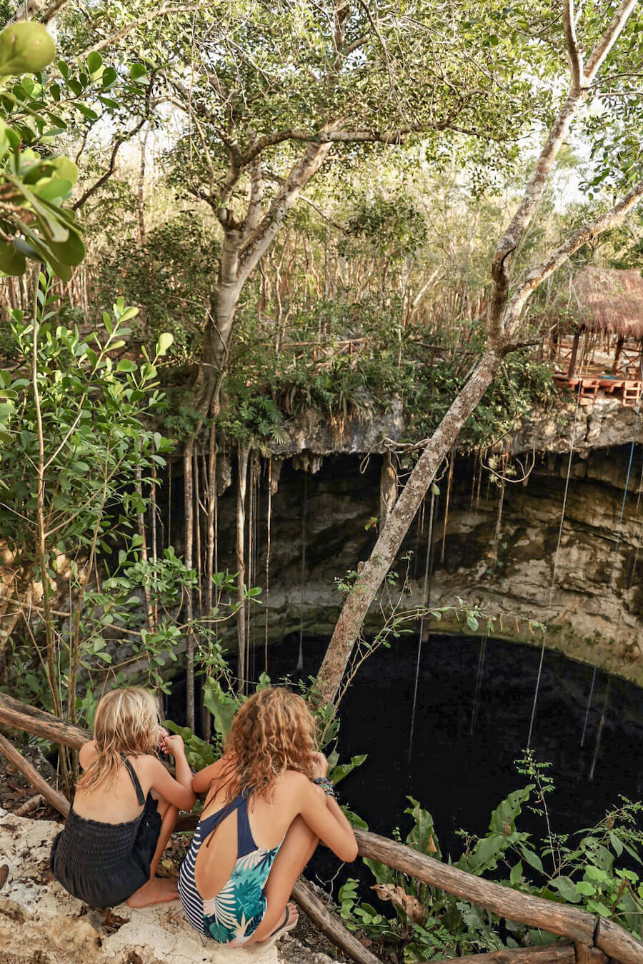 Two kids sit on a platform overlooking a cenote near Valladolid.