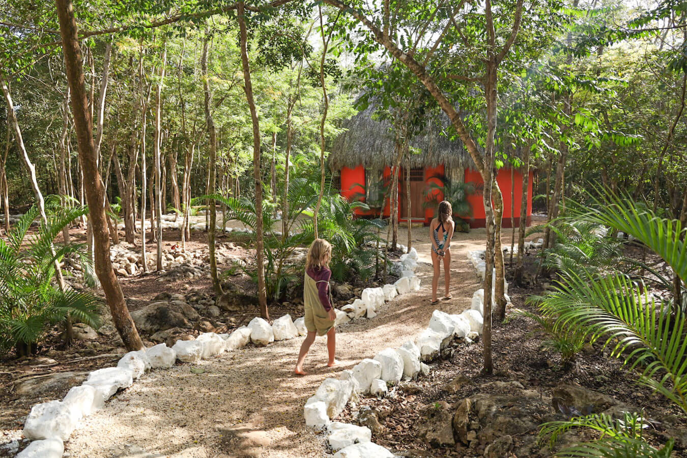 Children walk the path towards an orange bungalow at Cenote Secreto Maya.