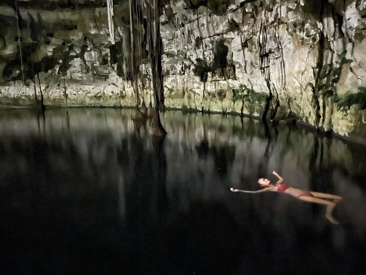 A woman swimming in the Secreto Maya Cenote in the night under the moon.