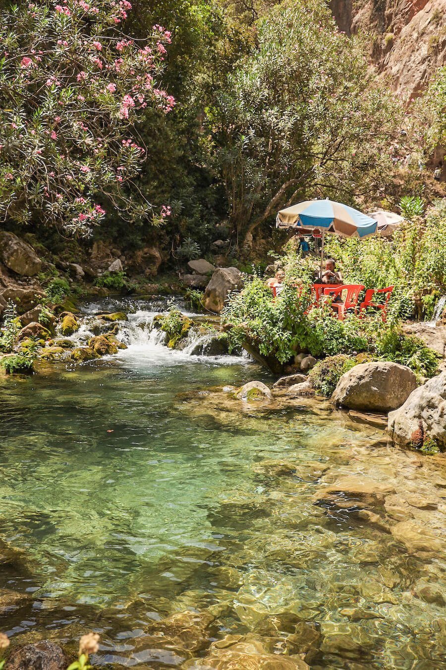 A family sit in the river in Akchour on the God's Bridge trail on a day trip from Chefchaouen, a popular activity on a Morocco itinerary