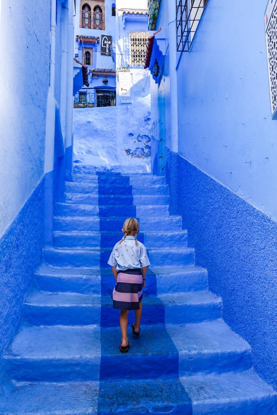 A young girl walks through the vibrant blue streets of Chefchaouen - while exploring the top things to do for a Chefchaouen itinerary Morocco