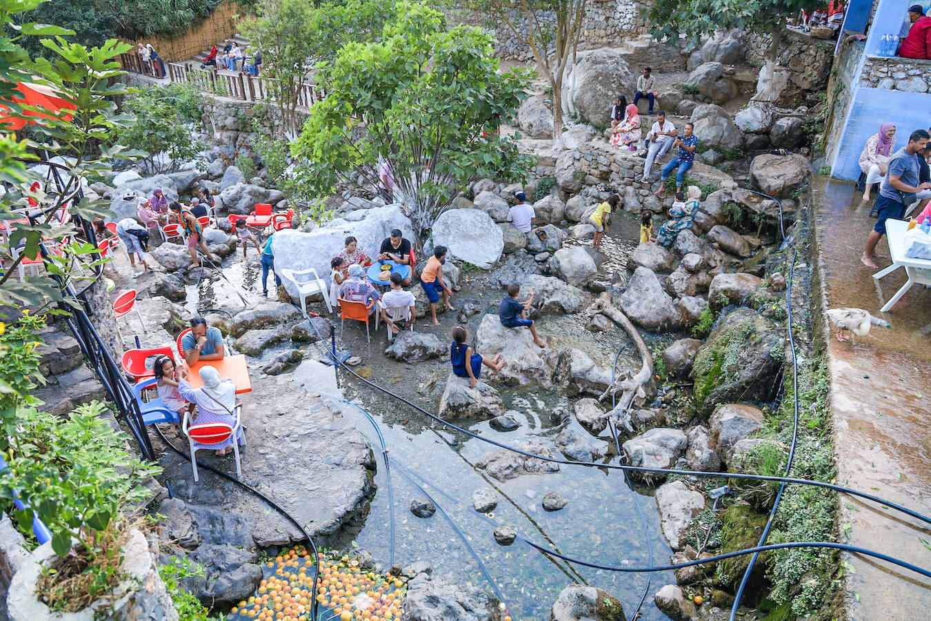 Holiday makers sit in the river near Chefchaouen drinking orange juice - one of the top things to do in Chefchaouen.
