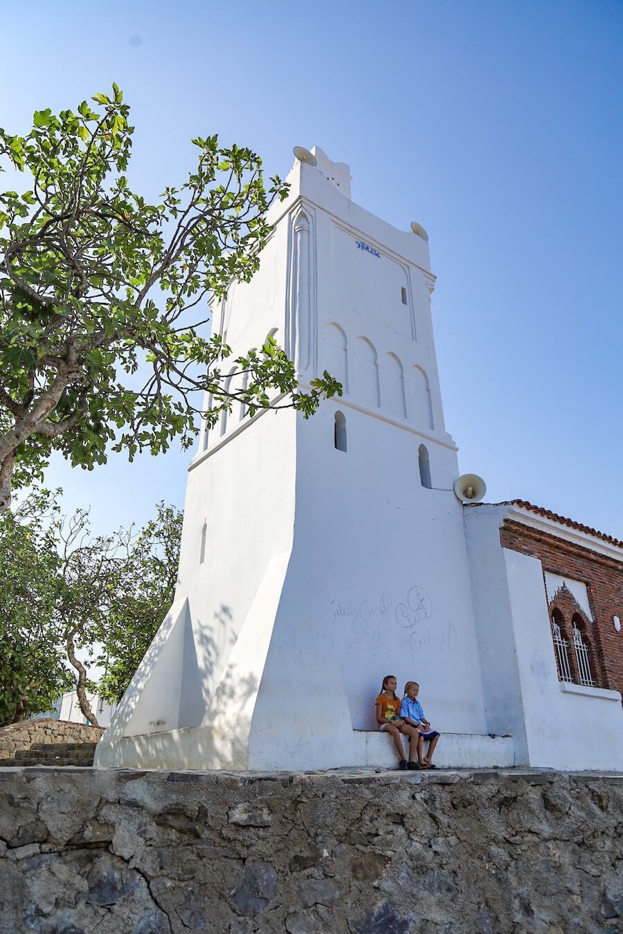 Two kids sit at the Spanish Mosque in Chefchaouen at sunrise - one of the top things to do when visiting Chefchaouen