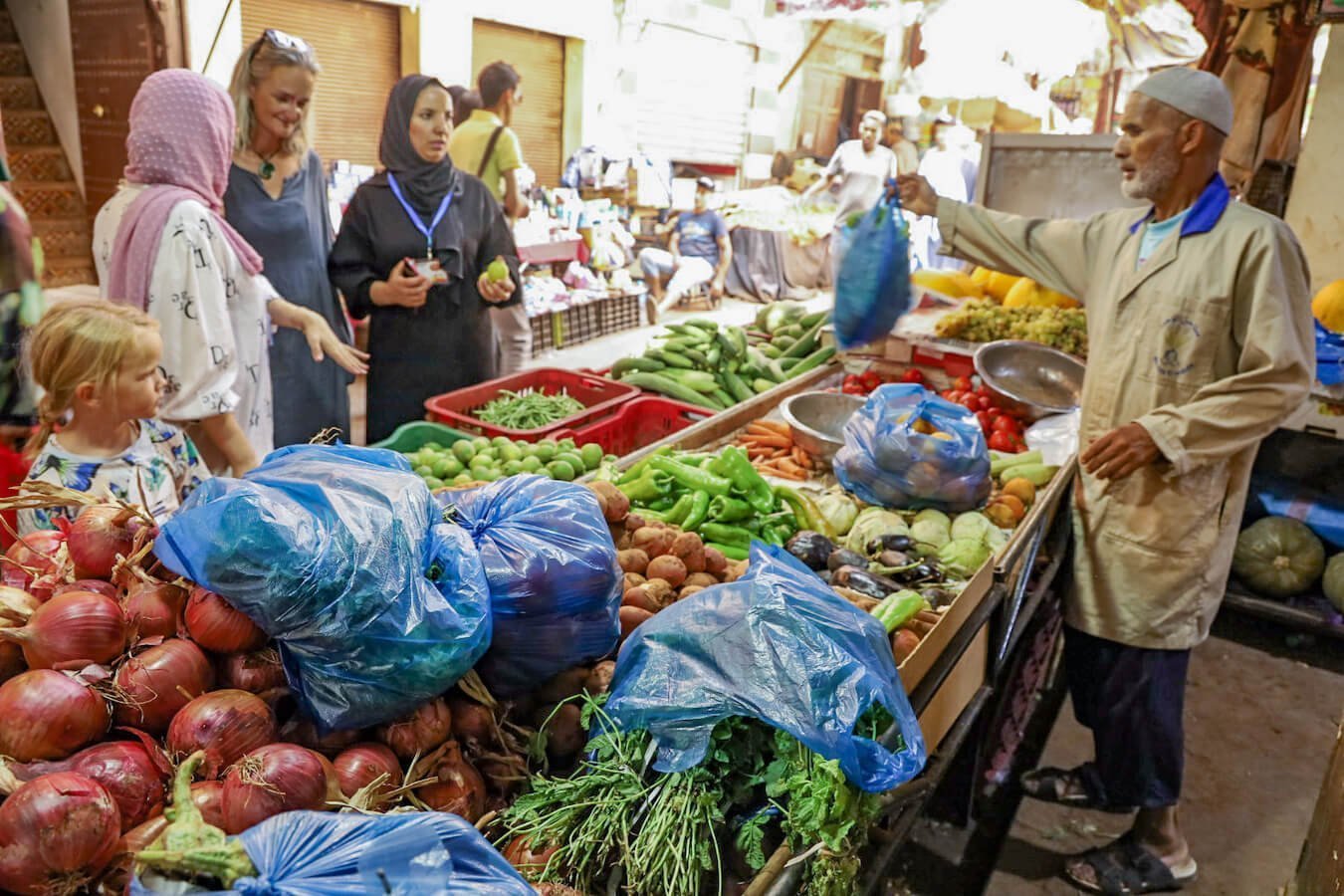 A family accompany a tour guide to buy vegetables in the medina, for a cooking class in Fes, Morocco.