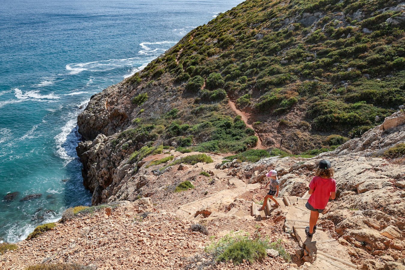 Kids walk down the steep trail stairs to Cova Tallada in Javea, Spain