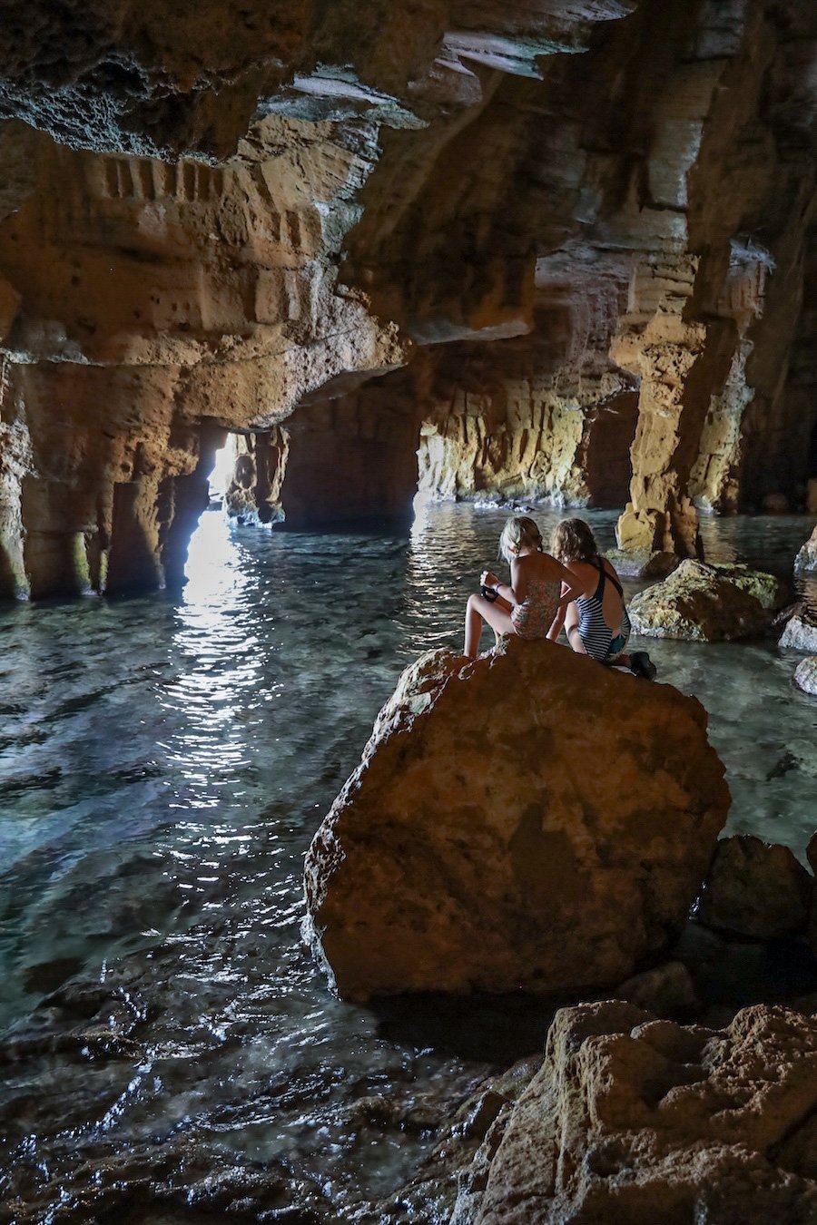 Kids sit on a large rock in a sea cave.