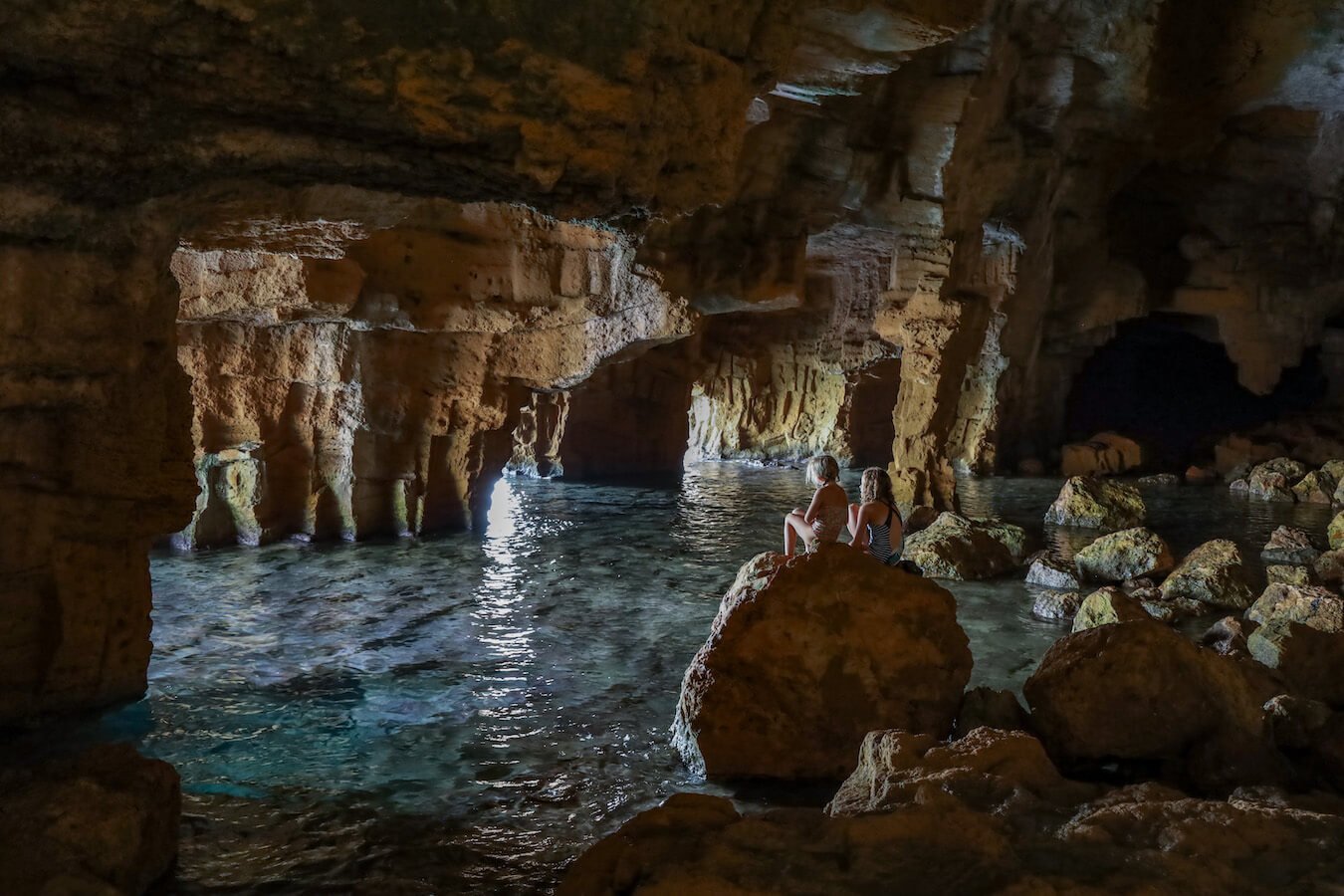Kids sit on a boulder in the sea cave of Cova Tallada near Denia and Javea in Spain.