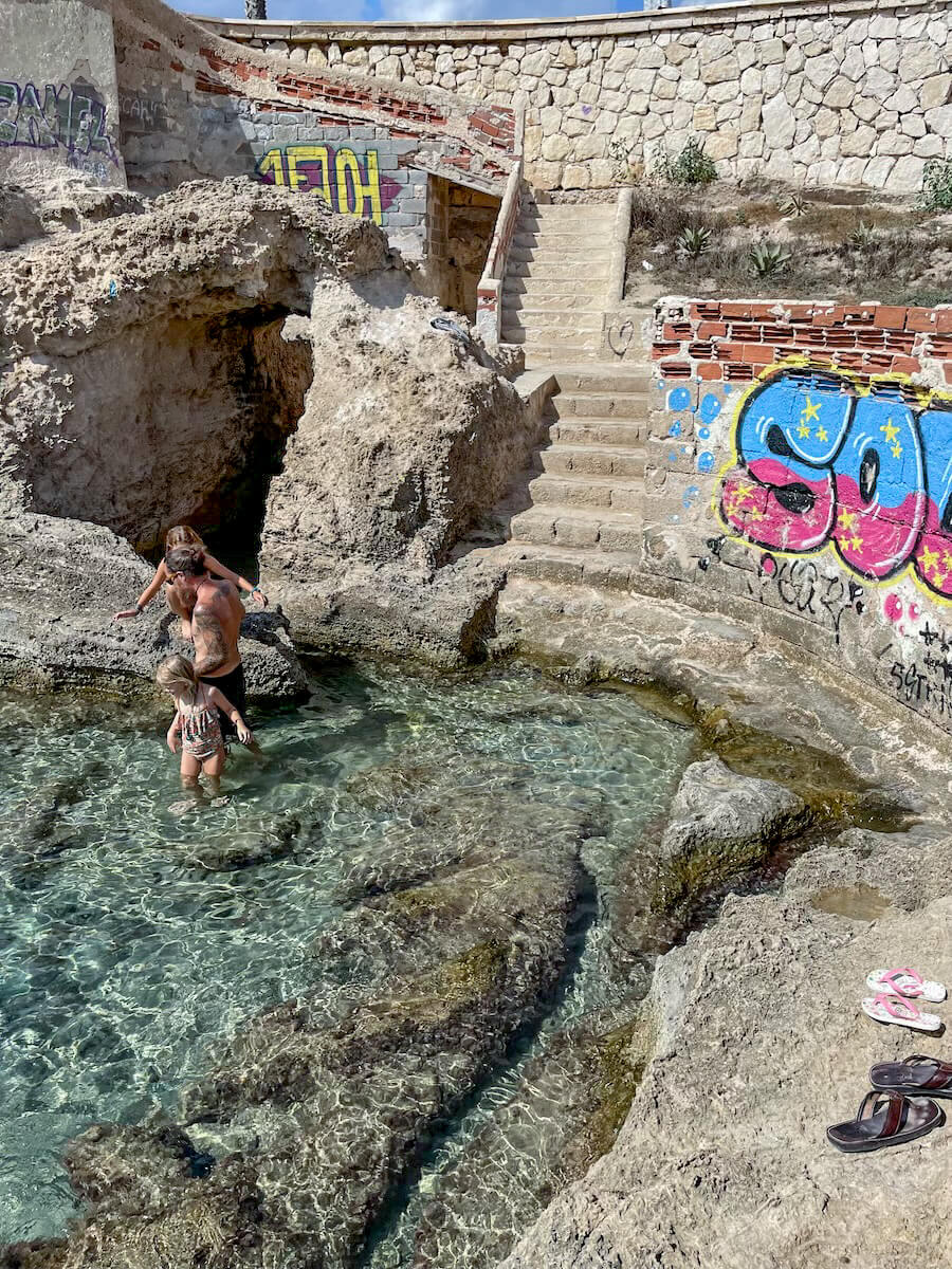 A father and kids on a day trip from Javea, swim in the Queen's Baths in Calpe, Spain