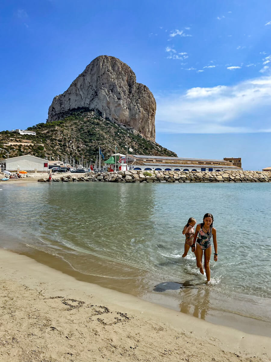 Kids on a day trip from Javea play on Cantal Roig Beach near the fishing port in Calpe, with the Calpe Rock, aka Peñón de Ifach, in the background