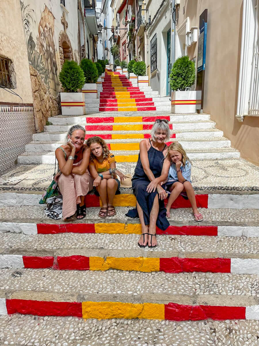 A family pose for a photo on the Spanish Flag painted steps of Carrer de Puchalt, while visiting the old town  in Calpe, on a day trip from Javea.