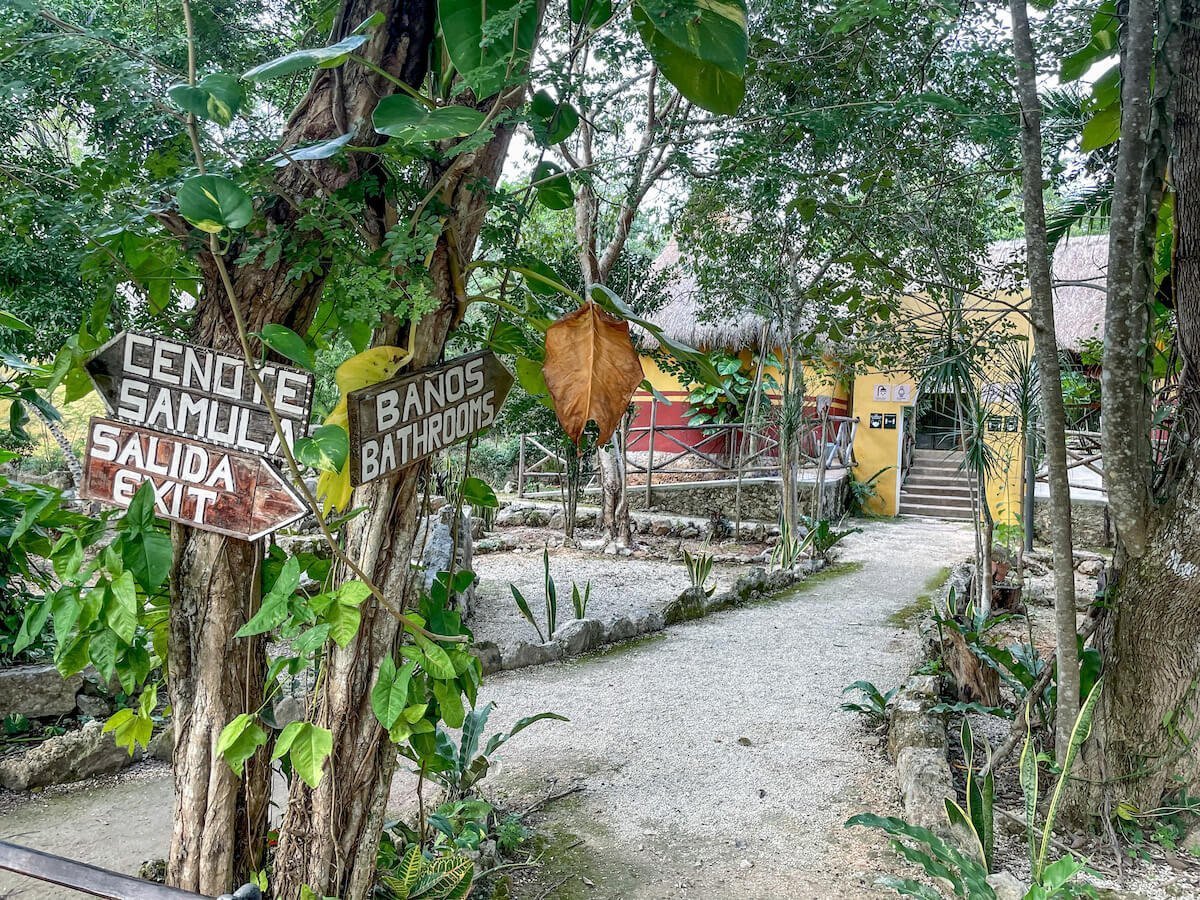 Signs at Dzitnup cenote pointing towards the bathrooms and changing facilities, as well as the Samula Cenote entrance.
