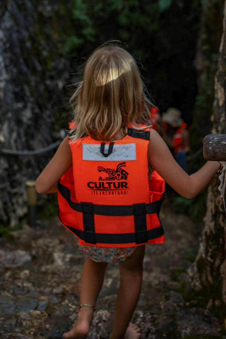 A child wearing a life jacket walks down the stair into the entrance of the Dzitnup Cenotes near Valladolid.