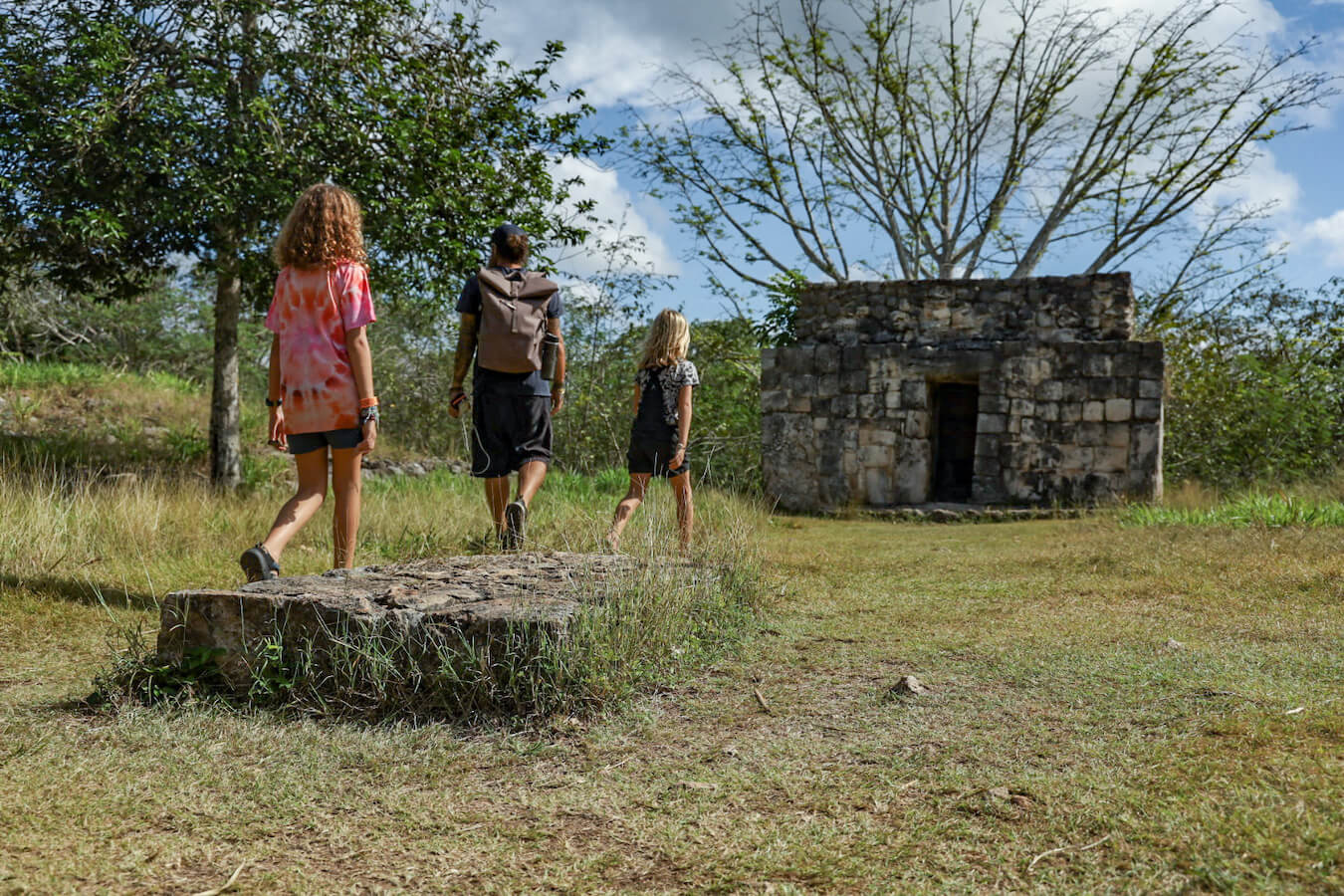 A family on a self-guided tour of Ek' Balam walk over the grassy platform of Structure 10