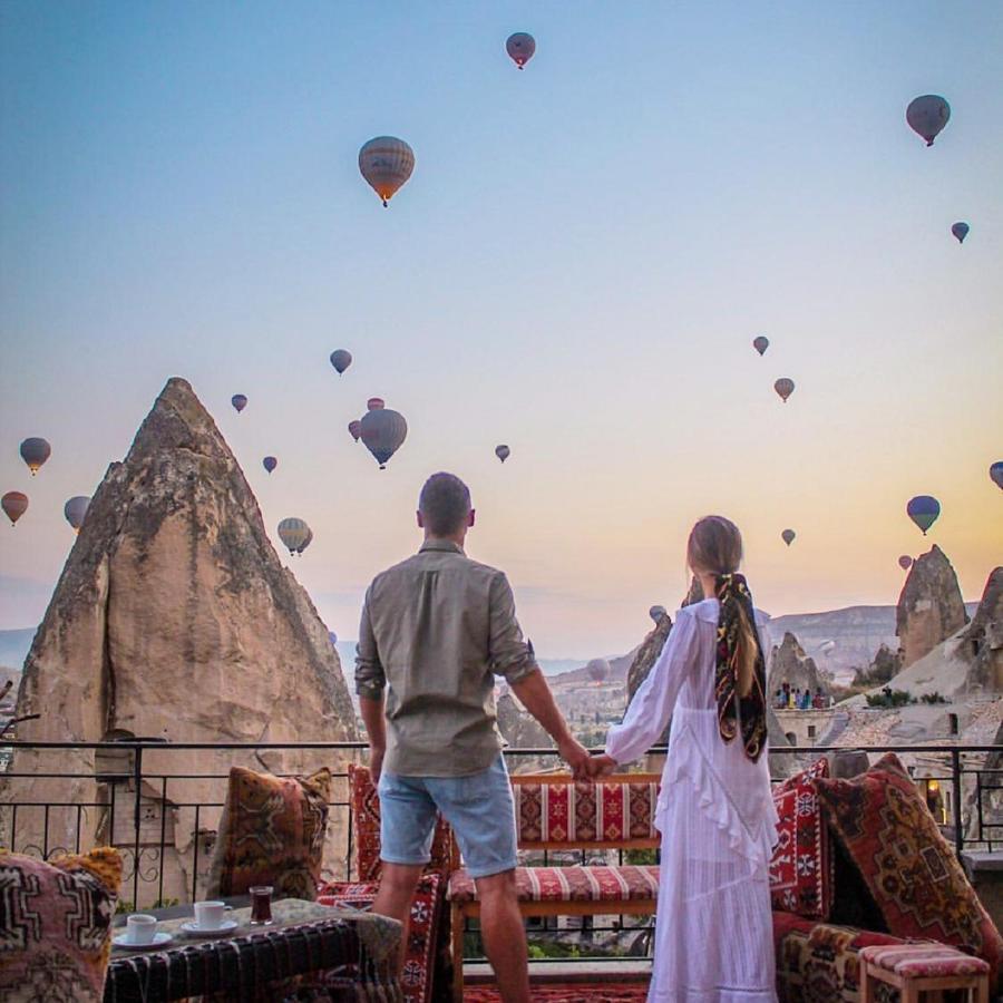 A couple stand on a terrace at Elite Cave Suites with views of a fairy chimney and hot air balloons.