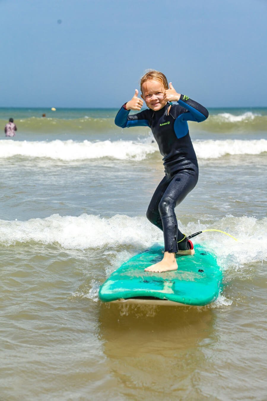 A child gives thumbs up while surfing.