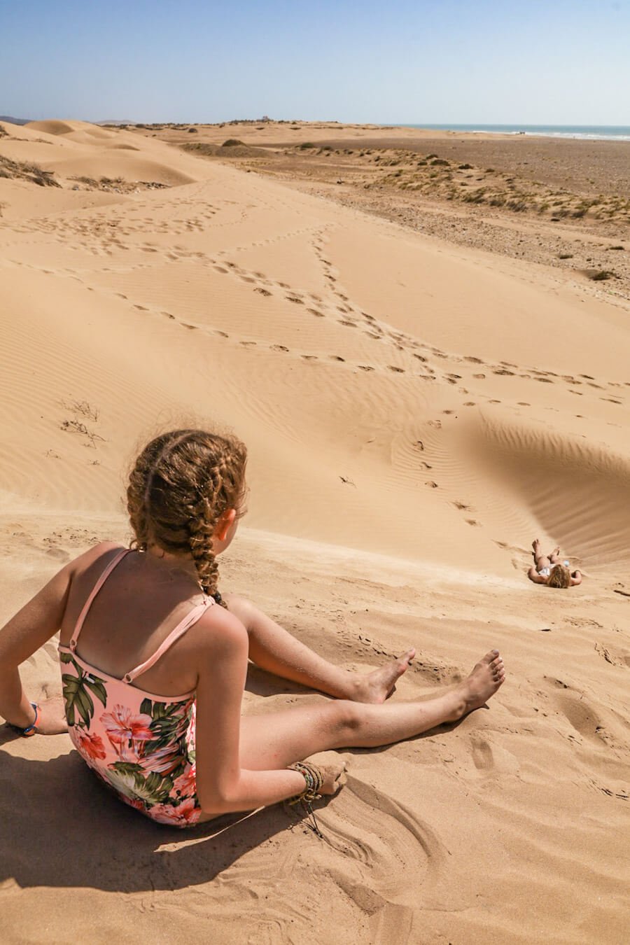 A child looks out from the sand dunes in Essaouira near Diabat - a travel guide