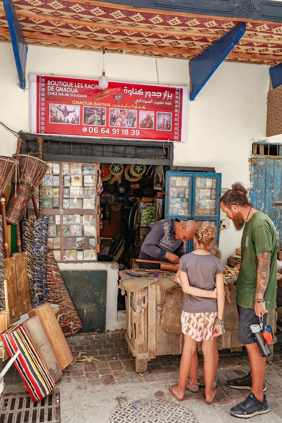 A family watch a man make Gimbri and Sintir for Gnaoua music in Essaouira Medina - A travel guide