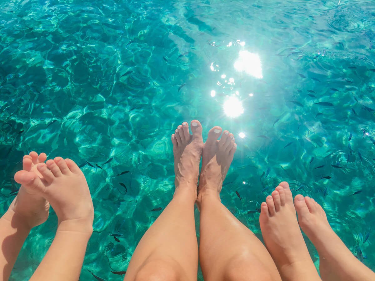 Family dip their feet in the Mediterranean on a beach vacation - packing list