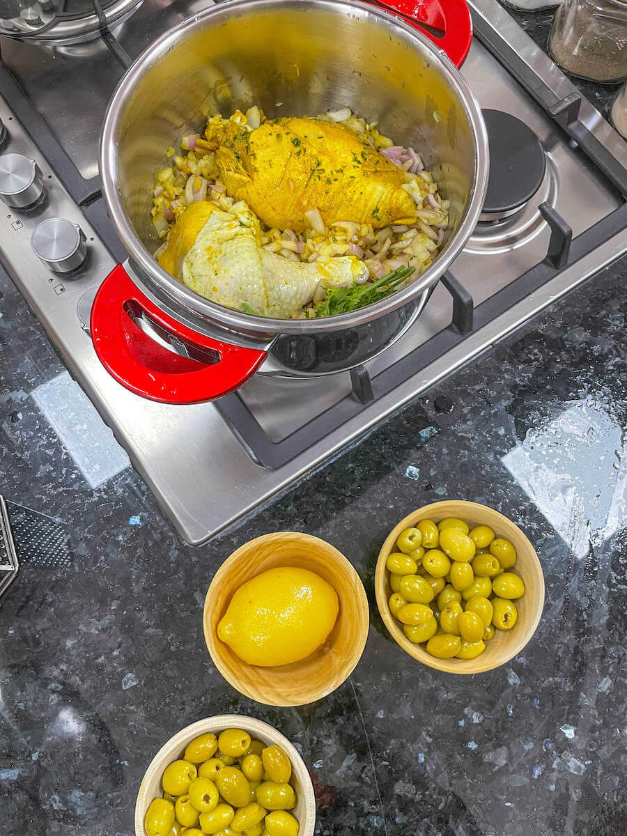 A chicken tagine cooks in a pot with a lemon and olives on the side