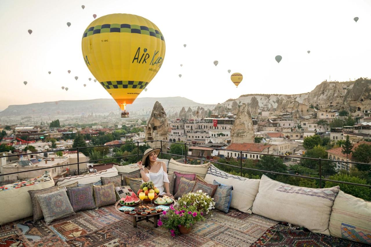 A woman sits on a beautifully styled terrace at Henna Hotel in Cappadocia with elevated views over Göreme and hot air balloons.