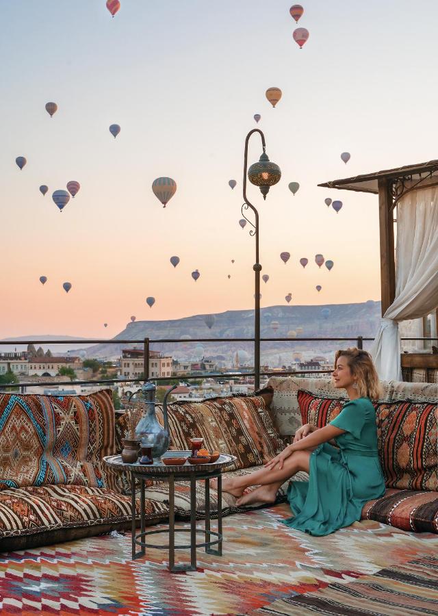 A woman sits on the rooftop of Hera Cave Suites admiring the hot air balloons as they fly over Cappadocia in the distance.