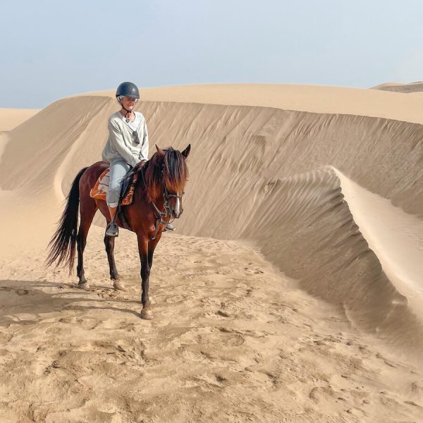 Woman on a horse riding tour in Essaouira in Morocco rides through the sand dunes.