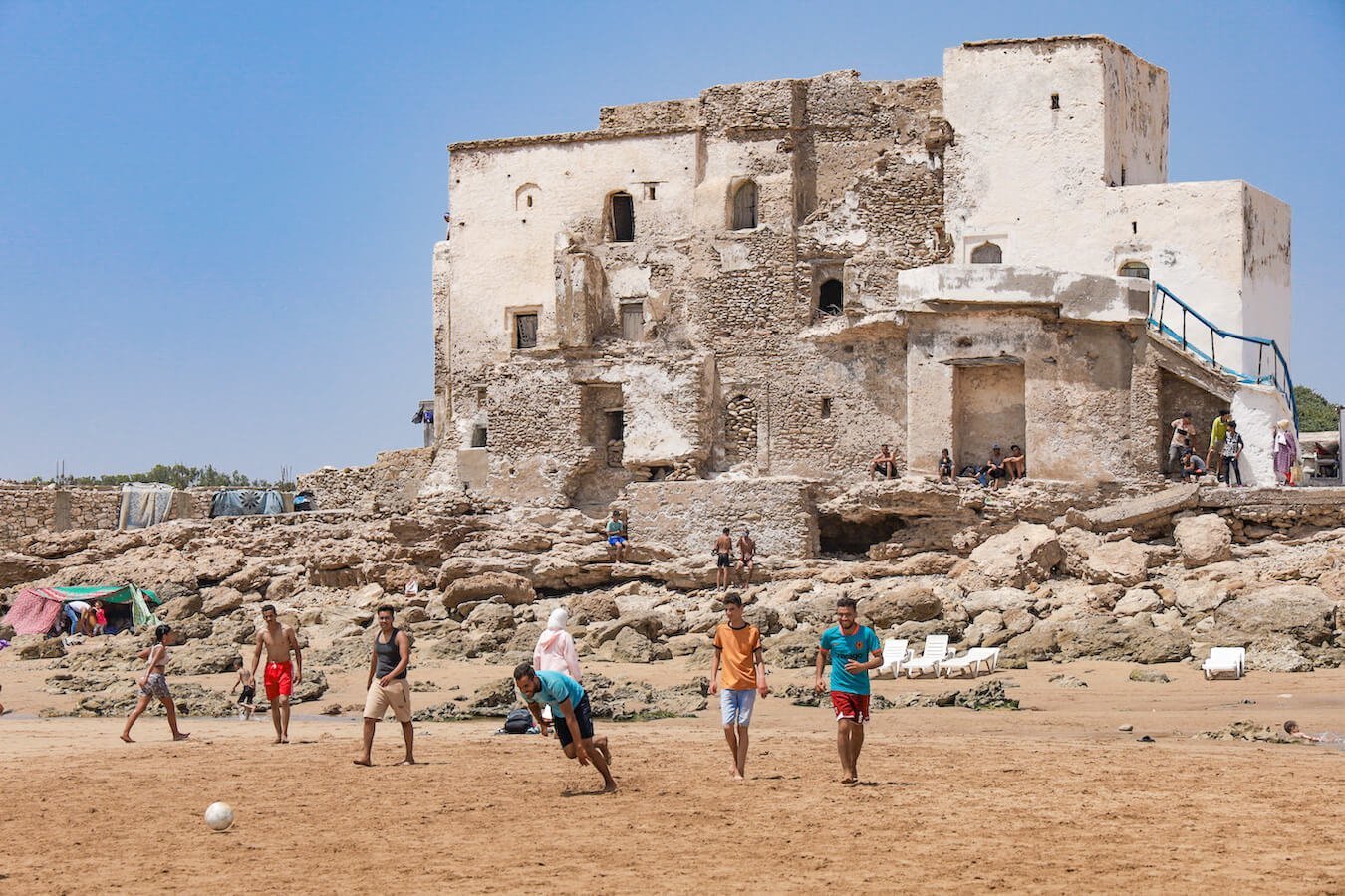 Men play football on the beach of Sidi Kouki with the shrine in behind them