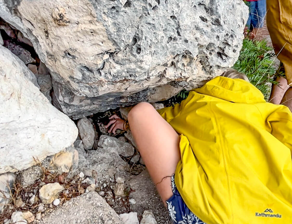 A child reaches under a rock to find a geocache