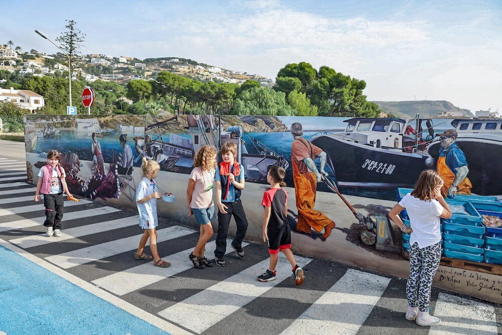 Kids walk past a mural at the Xabia / Javea Port.
