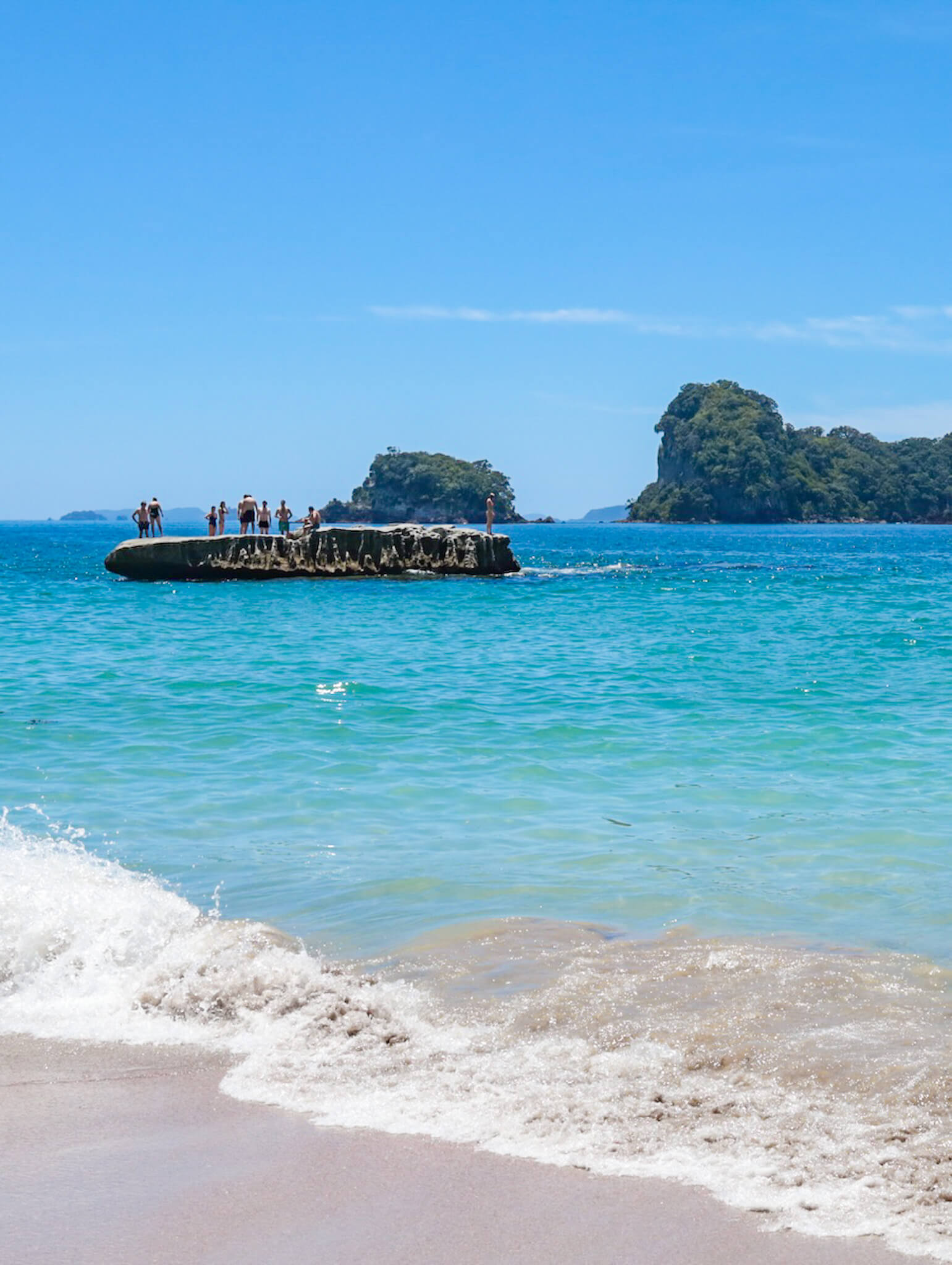 Beachgoers gather on the flat rock in the bay at Cathedral Cove