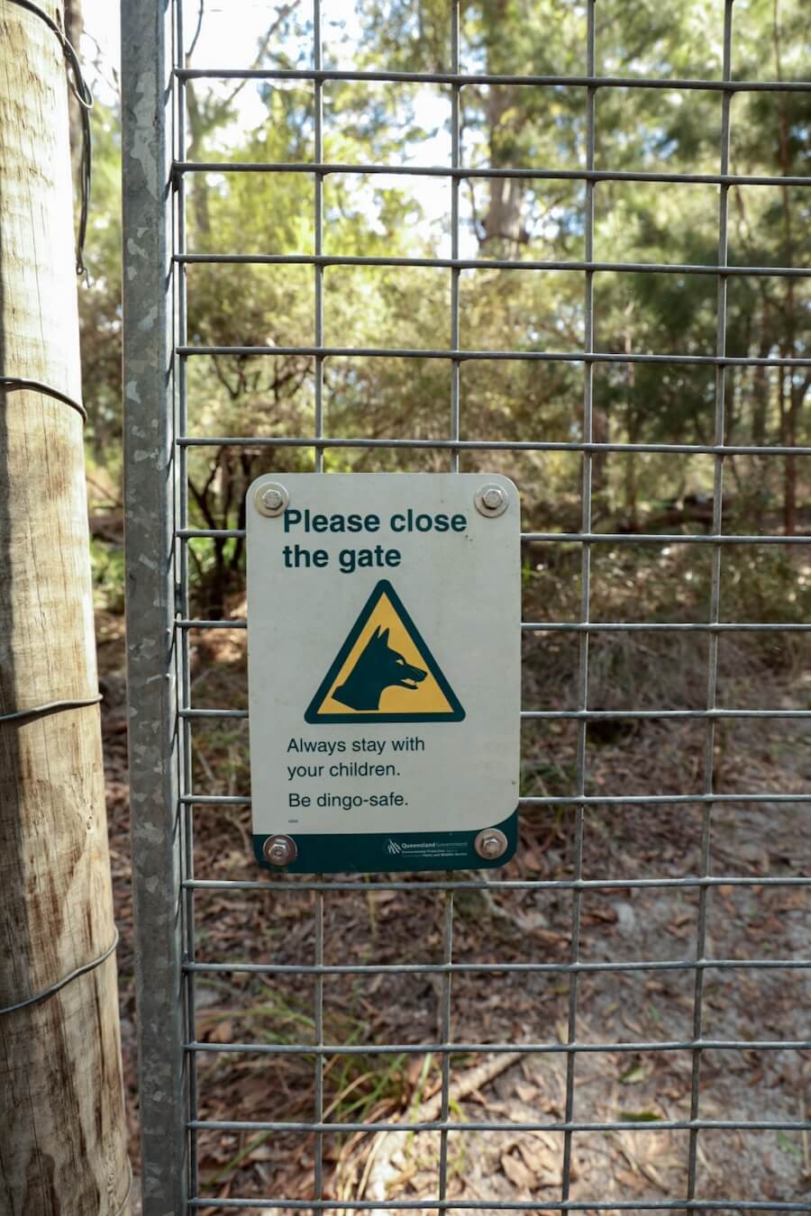 The dingo fence with sign reminding campers to keep the gate closed on K'gari Fraser Island